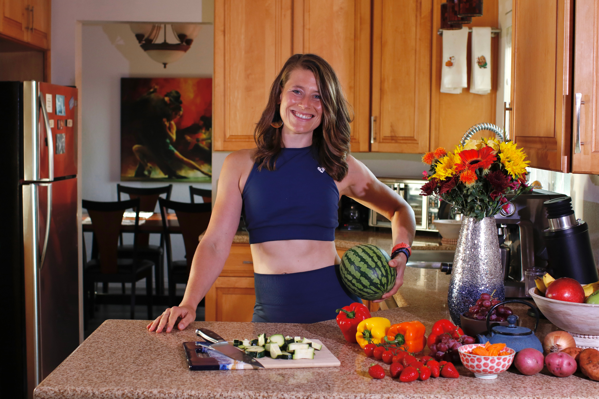 Lin in a blue outfit holding a watermelon surrounded by fresh produce